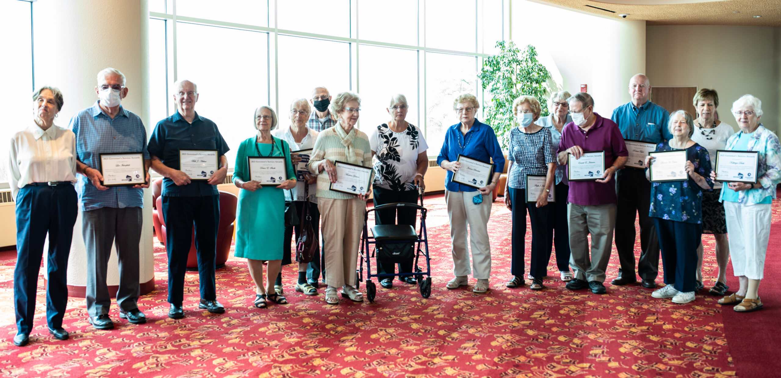 A group of elderly people standing in a row holding 8x10 framed awards they received 