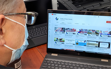 A man wearing a medical face mask looking at a video presentation library on a laptop screen