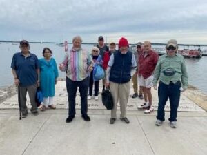 Un grupo de ancianos posa en un muelle de hormigón frente a un lago en un día nublado de verano.